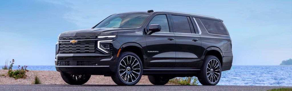 A black 2025 Chevrolet Suburban parked near a scenic shoreline near Seminole Chevrolet GMC in Seminole, OK, under a bright blue sky. 