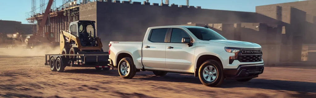 A white 2025 Chevy Silverado 1500 hauling construction equipment through a dirt road at an active construction site near Seminole, OK, during the day.