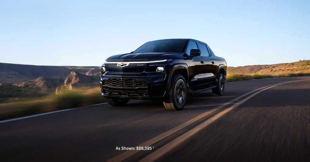 A black 2025 Chevy Silverado EV driving along a one-lane desert highway near Seminole Chevrolet in Oklahoma, highlighting its rugged design and electric capability.