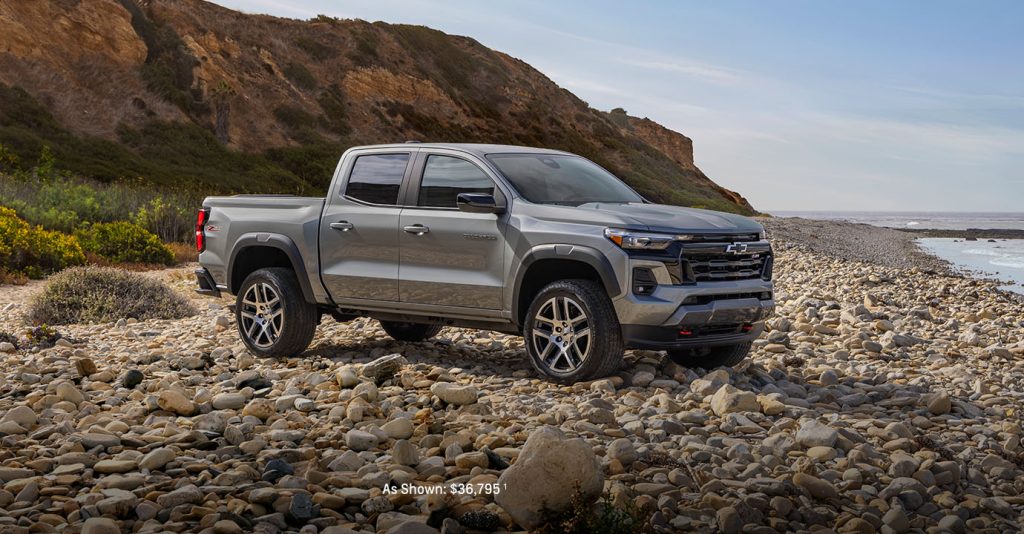 2025 Chevy Colorado parked on rugged shoreline rocks with a scenic mountain backdrop.