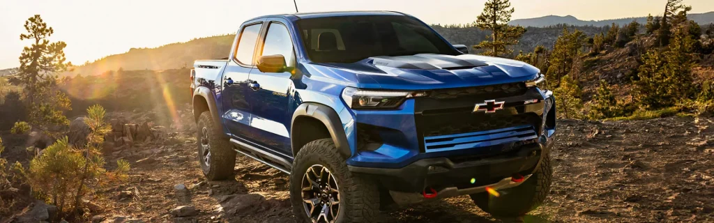 Blue Chevrolet Colorado ZR2 off-road truck parked on rocky terrain at sunset.