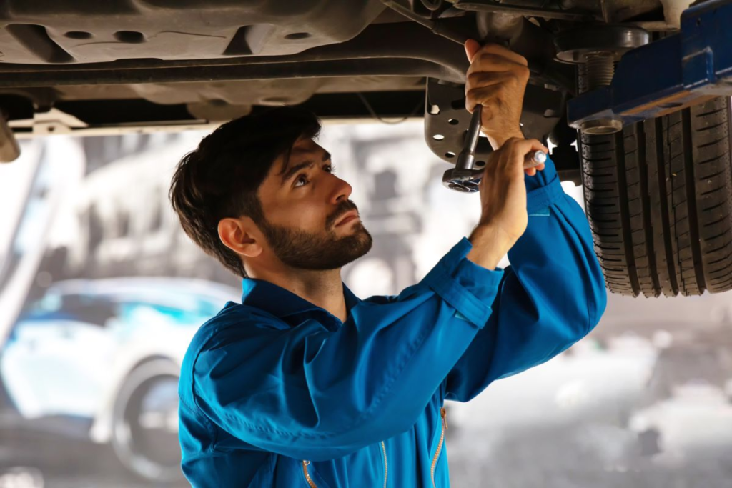 Auto technician inspecting and repairing a vehicle underneath with a wrench in a service bay.
