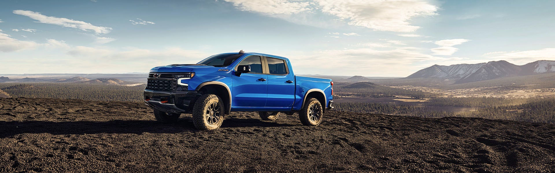 Blue 2025 Chevrolet Silverado 1500 driving through black sand and dirt in a desert landscape near Seminole, OK, during daylight.