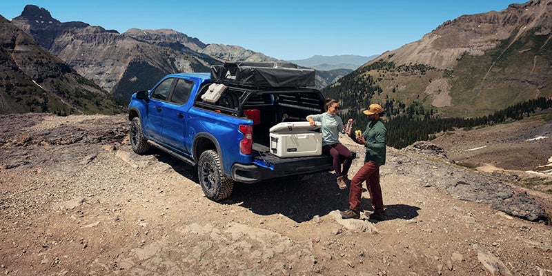 A family hauling supplies out the bed of a blue 2025 Chevrolet Silverado 1500 parked in a desert landscape near Seminole, OK, during daylight.
