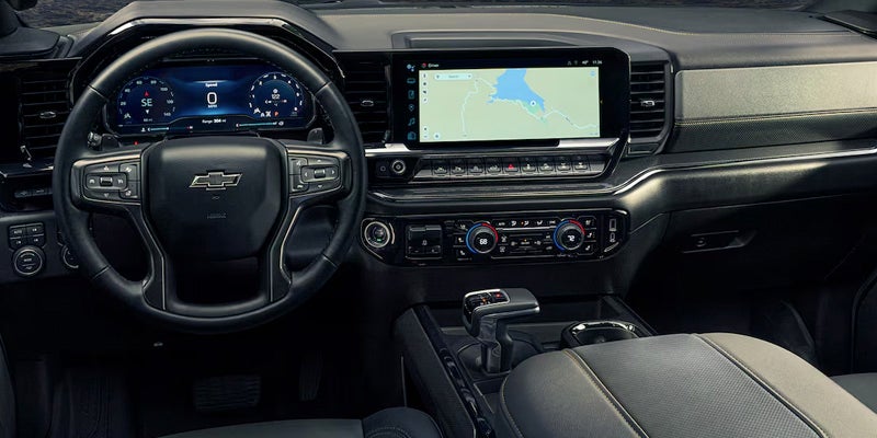 Interior view of the 2025 Chevrolet Silverado featuring gray and black leather seats, a large infotainment display, and the Chevy digital driver dash.