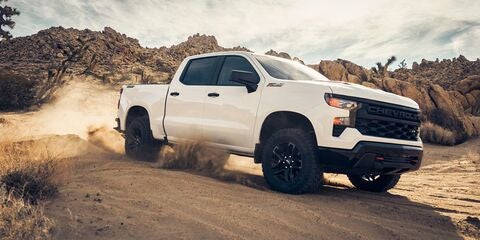 A white 2025 Silverado 1500 driving through a dessert terrain on a sunny day with tall rocks in the background near Seminole, OK.